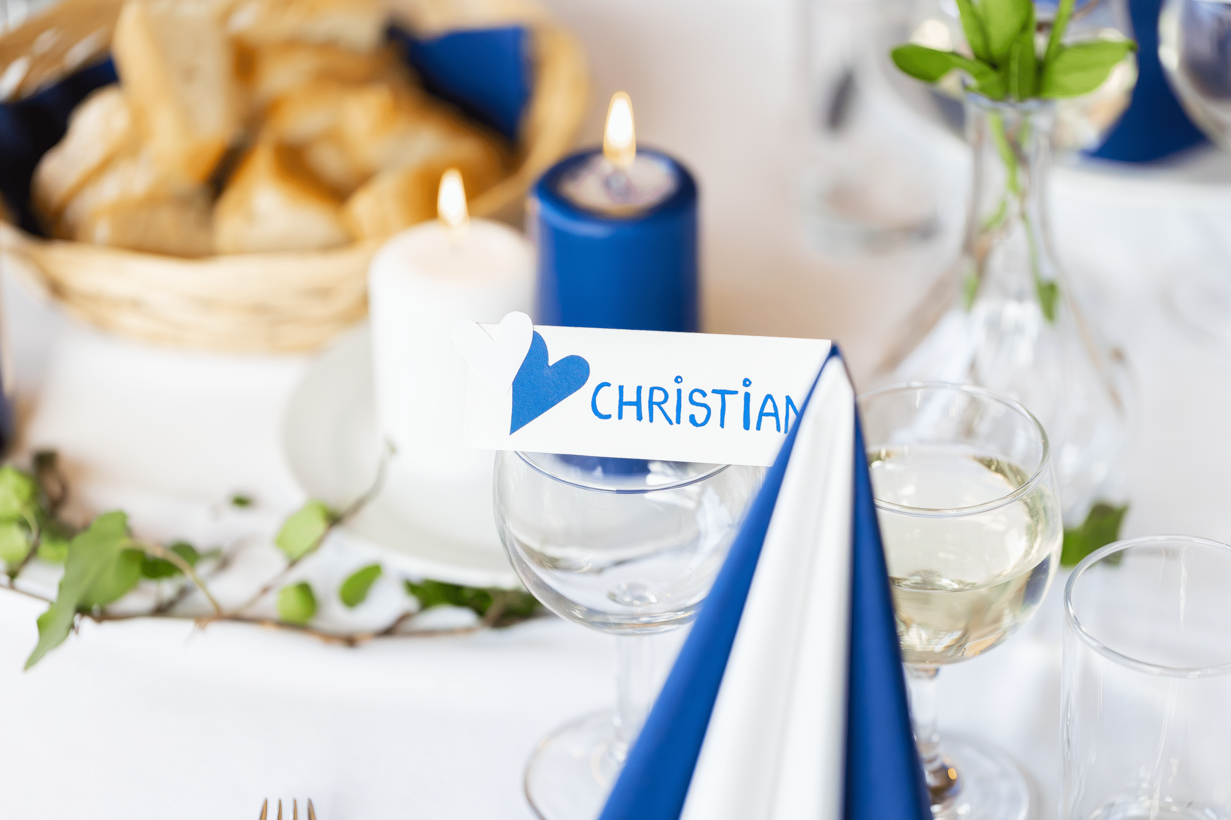 Konfirmationsfotografen har fotograferet en bordopstilling i blå/hvide farver tæt på. Der er stillet skarpt på en vinglas med et bordkort stående på.