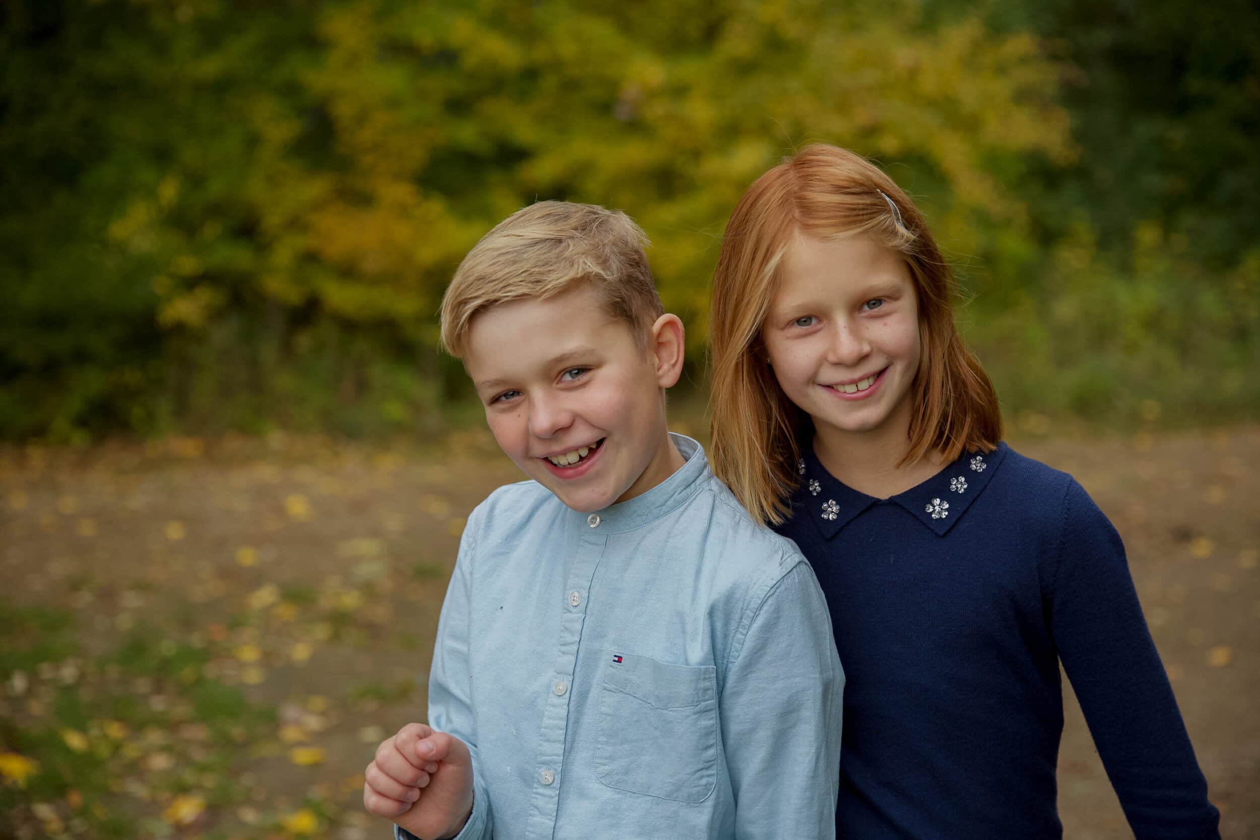 Opstillet billede af tvillinger (dreng og pige), står tæt ved hinanden med skoven som baggrund