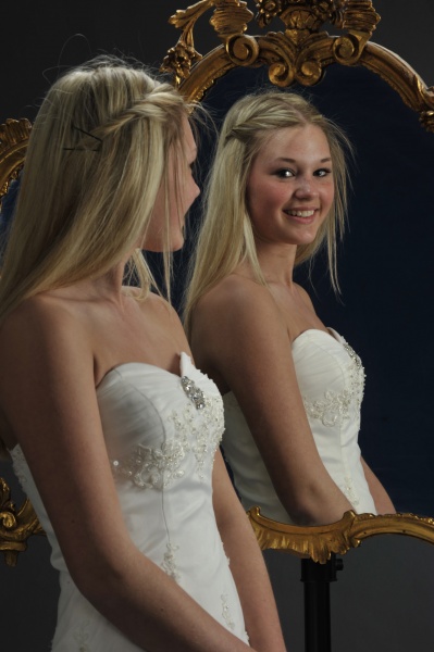 Festfotograferne har her fotograferet en kvindelig konfirmand. Du ser hende stå foran og kigge ind i et spejl. I spejlet kan du så se hendes ansigt